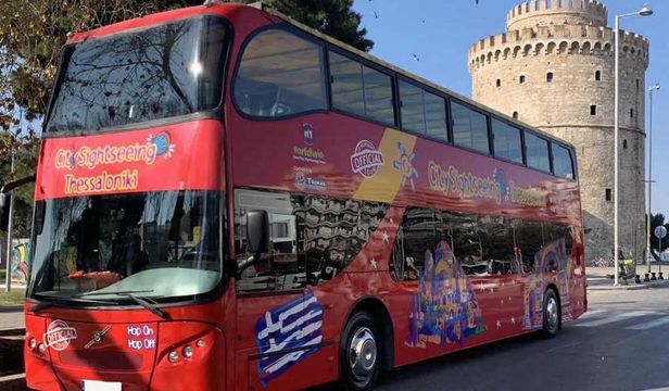 Bright red City Sightseeing Thessaloniki Hop-On, Hop-Off bus gracefully glides through the streets, revealing the beauty of Thessaloniki.