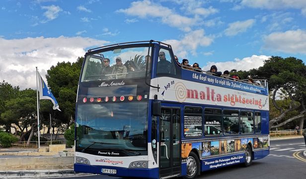 Vibrant blue Malta Sightseeing bus navigating through the streets, brimming with thrilled passengers, creating an unforgettable experience.
