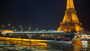 Nighttime Seine River cruise, Eiffel Tower illuminated backdrop. Enchanting atmosphere as cruise ship sails with happy passengers.