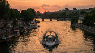 A stunning photograph of a cruise ship in the peaceful Seine River with the most beautiful sunset serving as the perfect background.
