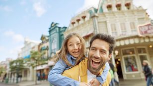 A joyful photograph of a father daughter duo in front of Disneyland Paris, excited to experience all the fun rides and attraction.