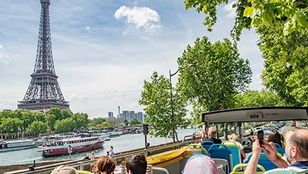 Sightseers enjoying the picturesque view of the Eiffel Tower and a cruise ship while taking photos from their comfortable bus seats.