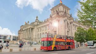 A vibrant hop-on, hop-off bus moves through the streets of Berlin, offering tourists an immersive experience of the city's bustling atmosphere.