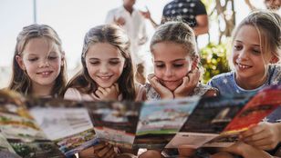 A group of children eagerly engrossed in their travel guide book, embracing the excitement of the moment with wide-eyed curiosity.