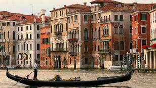 Scenic Venice canals with a gondolier gliding through, framed by picturesque row houses, offer a quintessential Venetian experience.