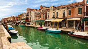 Tourists stroll along Murano's canal-side path, admiring the picturesque scenery and charming atmosphere of the island.