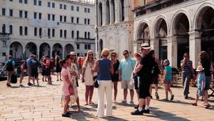 A photo captures tourists gathered at Venice's iconic St. Mark's Basilica, admiring its beauty and discussing its history.