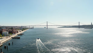 A thrilling sight of a Hop-On Hop-Off boat splashing along Lisbon's river, framed by the iconic bridge, encapsulating the city's charm.