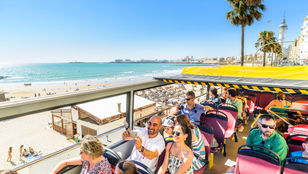Excited tourists capturing memories on a City Sightseeing bus in Cadiz, admiring the beach views and taking selfies along the way.