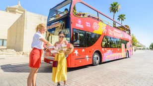 Bus hostess providing information to a young traveler against the backdrop of City Sightseeing Cordoba Hop-On, Hop-Off bus.