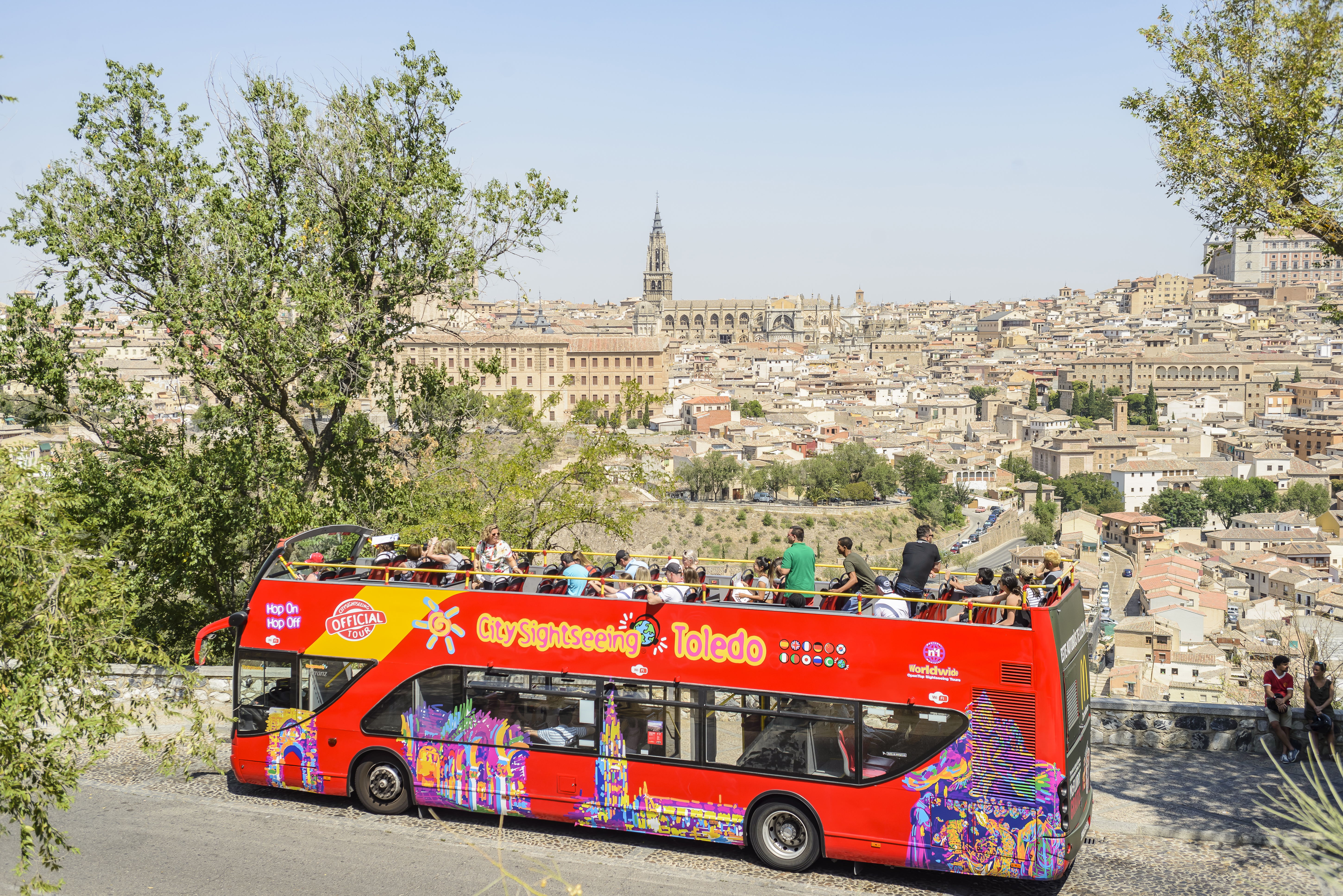 Excited passengers on a bright red City Sightseeing Toledo Hop-On, Hop-Off bus, savoring the cityscape as it glides through the charming streets.