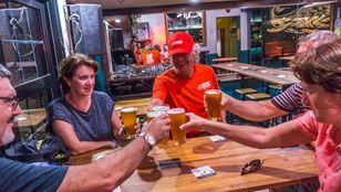 At the bar table, a group of tourists cheerfully raise their beer glasses, enjoying a lively and fun-filled moment together.