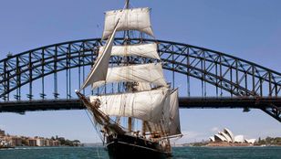 A Tall Ship sails gracefully, framed by the iconic Sydney Harbour Bridge, a picturesque blend of maritime elegance and urban grandeur.