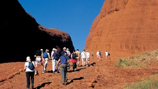Tourists stroll through Mutitjulu, immersing themselves in the timeless wonder of Australia's majestic Outback landscape.
